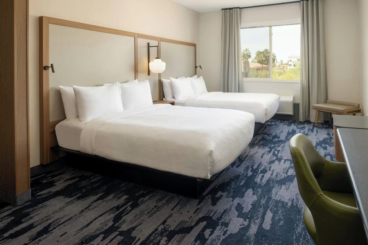 A hotel room with two beds, a desk, and a chair.