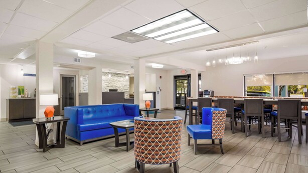 Un hall d’hôtel avec un canapé bleu, des fauteuils à motifs, un coin café et un comptoir de réception.
