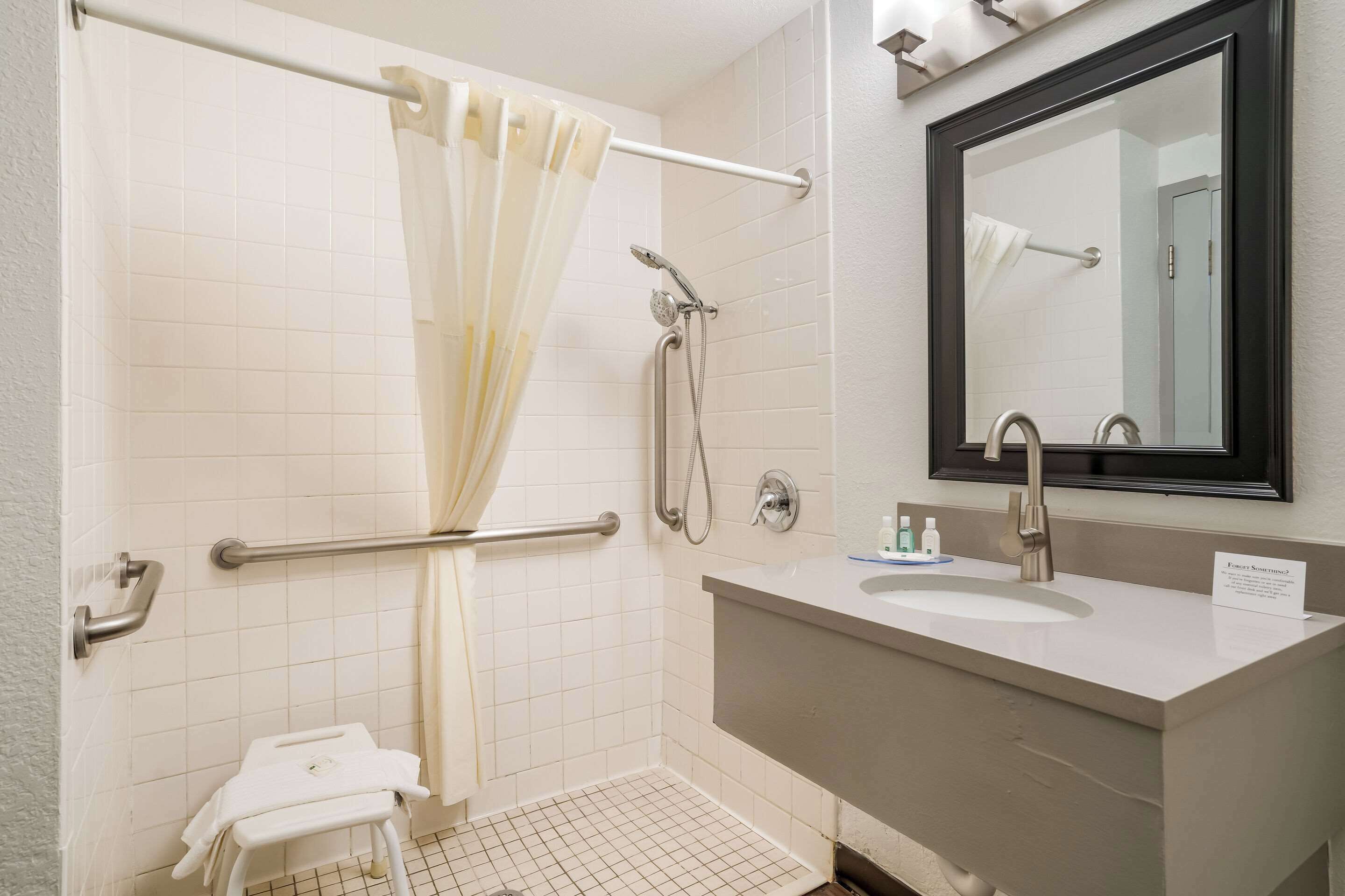 A bathroom with a shower, a sink, a mirror, and a towel rack.
