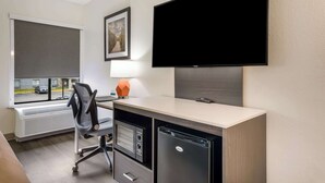 Une chambre d’hôtel équipée d’un bureau, d’une chaise, d’une télévision, d’un radiateur et d’une fenêtre donnant sur la rue.
