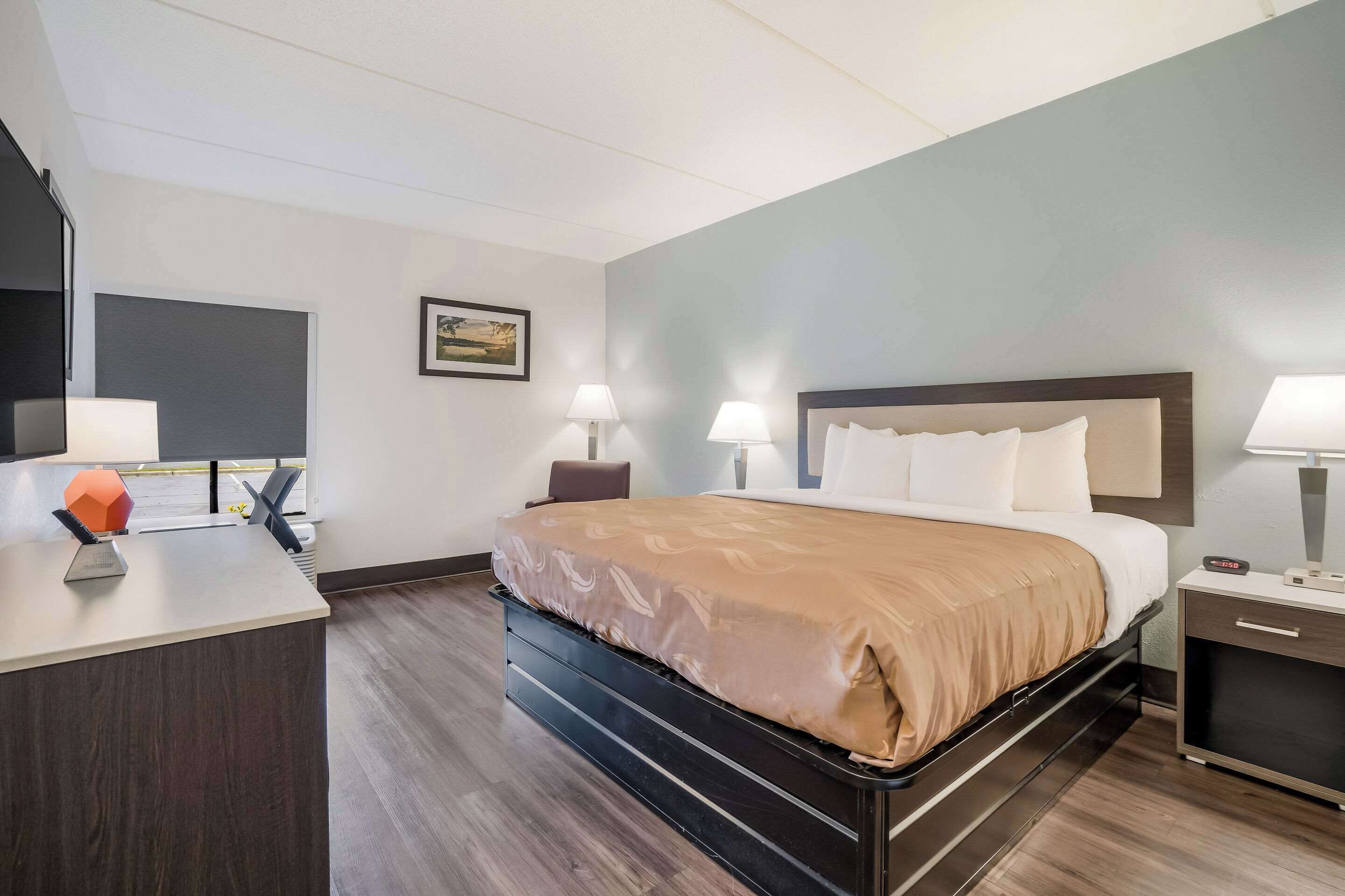 Una habitación de hotel con una cama, mesitas de noche, un escritorio y una silla.