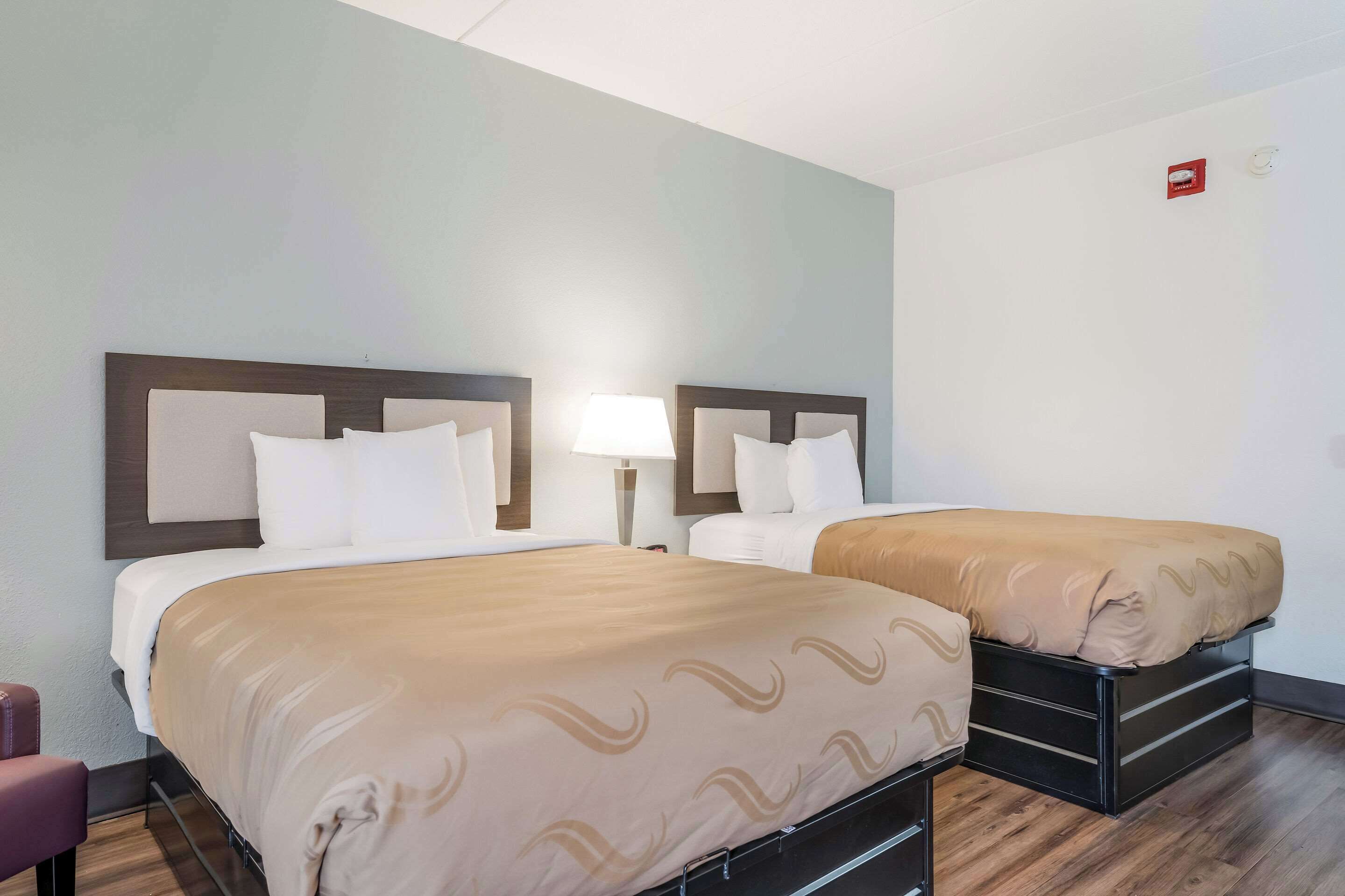 Une chambre d’hôtel avec deux lits, chacun doté d’une tête de lit, d’une table de chevet avec une lampe et d’un plancher en bois.