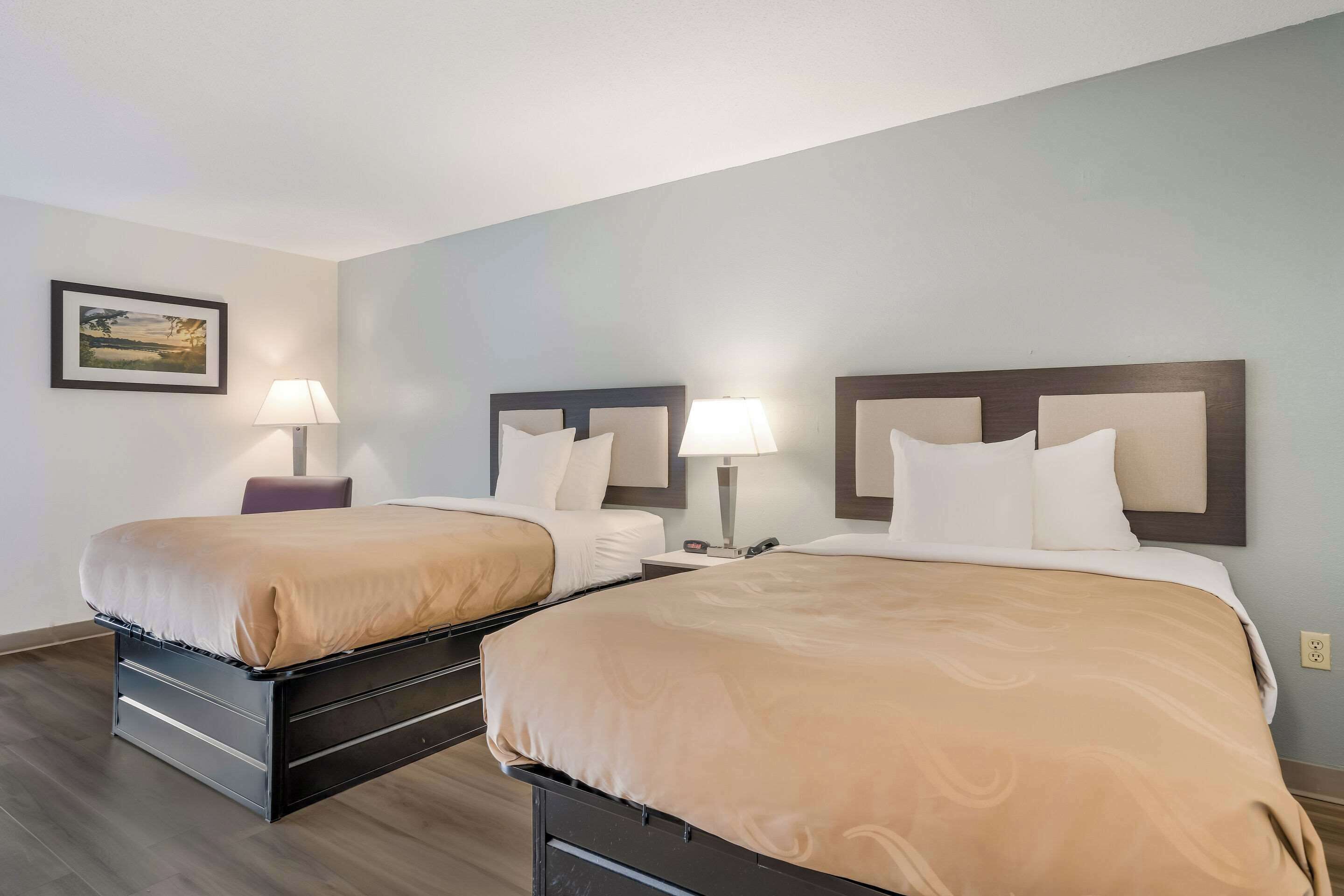 A hotel room with two beds, each with a wooden headboard, white bedding, and bedside lamps.