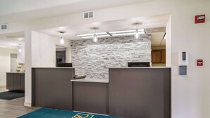 Un espace d’accueil avec un mur en pierre, un paillasson bleu orné du logo « QUALITY INN » et un détecteur d’incendie fixé au mur.