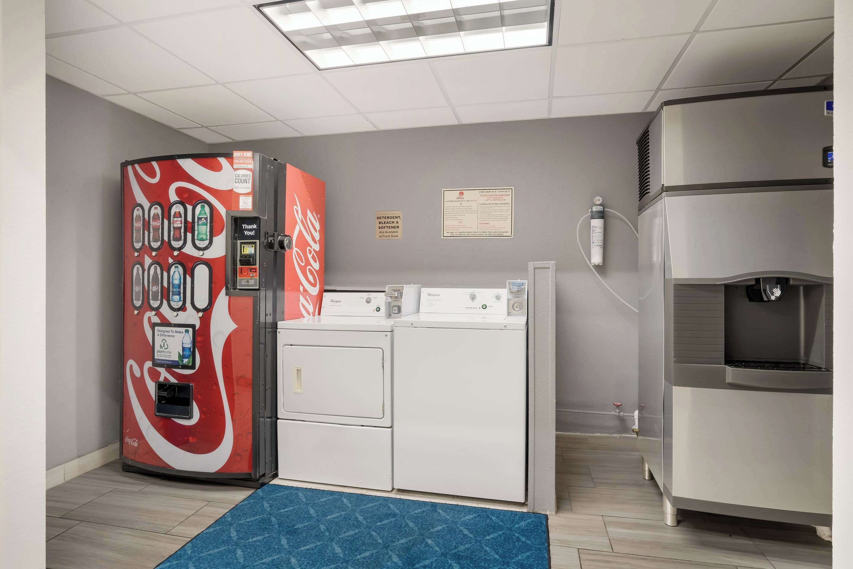 Un área de lavandería con una máquina expendedora de Coca-Cola, dos secadoras y un dispensador de agua.