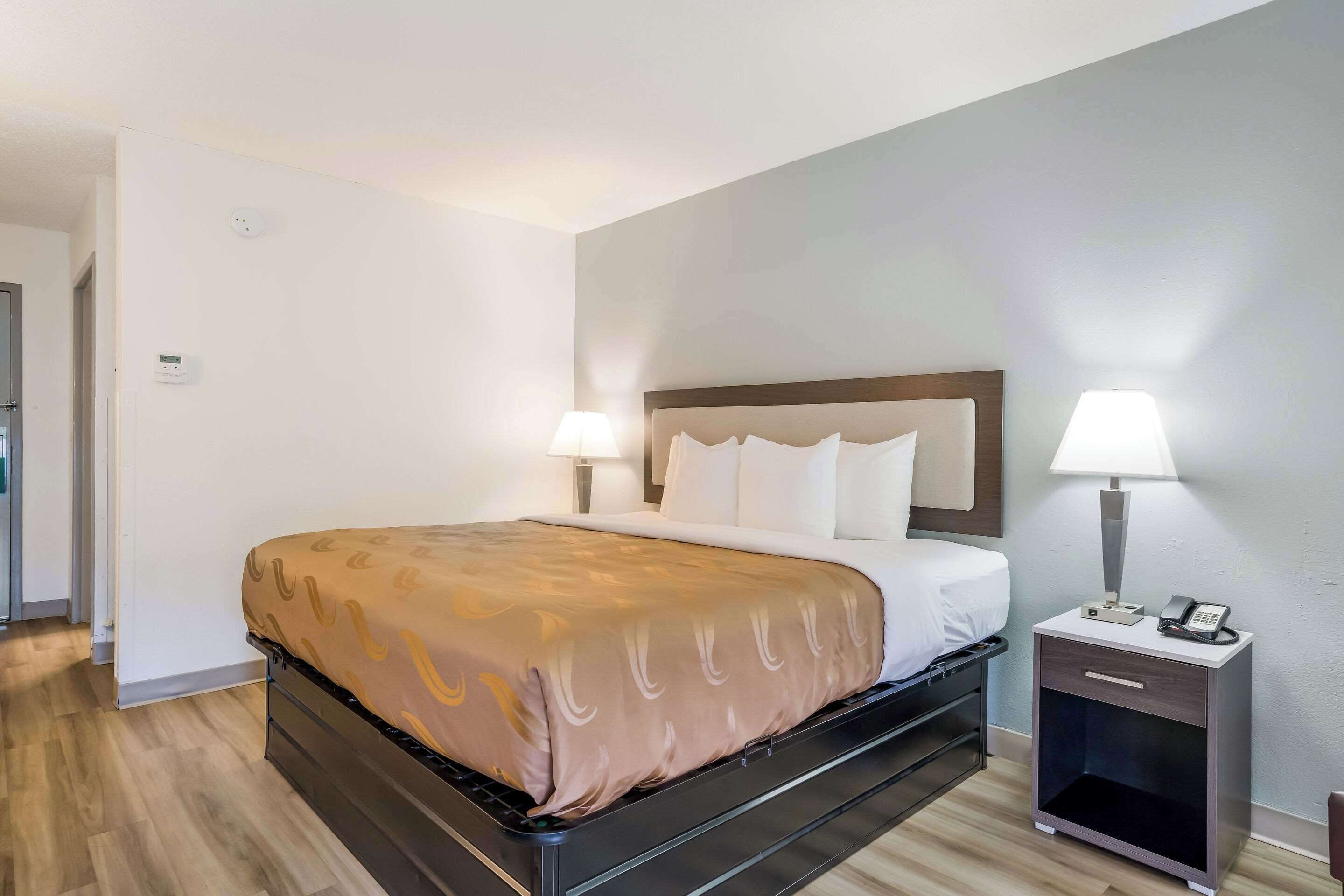 Una habitación de hotel con una cama, lámparas de noche, una mesita de noche y una puerta.