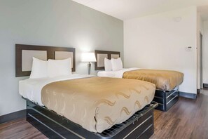 A hotel room with two beds, a nightstand with a lamp, and a wooden floor.
