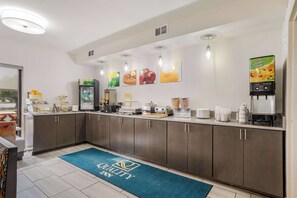 A hotel kitchen with a coffee machine, a juice dispenser, and a refrigerator.