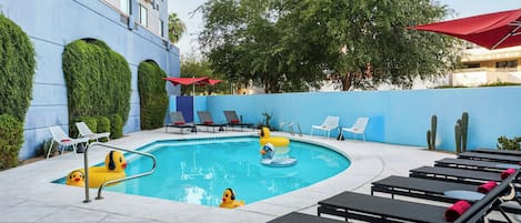Zona de piscina amb gandules, piscina i edifici amb façana blava.
