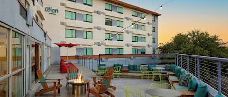 Un área de estar al aire libre con sillas de madera y neón, un brasero y vistas del edificio del hotel.