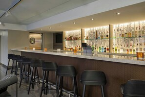 A bar area with a long counter, multiple stools, and a wall of liquor bottles. - Aloft by Marriott Scottsdale (Scottsdale)