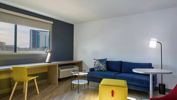 Una sala de estar moderna con un escritorio, un sofá azul, un reposapiés amarillo, una silla roja y una mesa redonda.