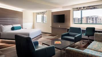 Una habitación de hotel moderna con una cama, un televisor de pantalla plana montado en la pared, un espacio de descanso con una mesa de centro y un amplio ventanal con vistas a la ciudad.