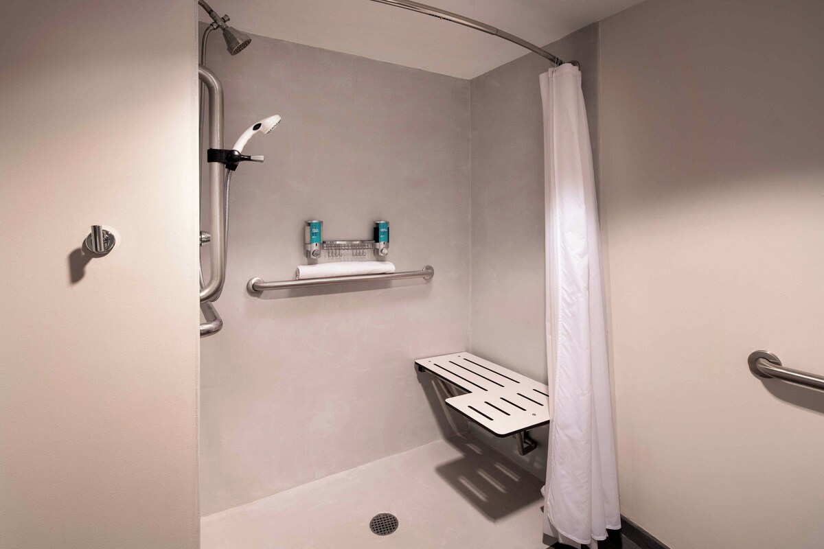 A modern shower area with a handheld showerhead, a white shower curtain, and a grab bar.