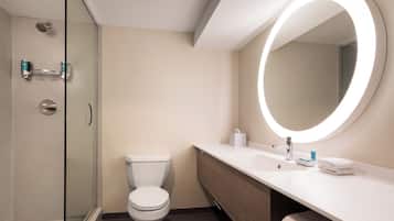 Un baño moderno con cabina de ducha de vidrio, inodoro, tocador con lavamanos y un espejo grande con luz circular.
