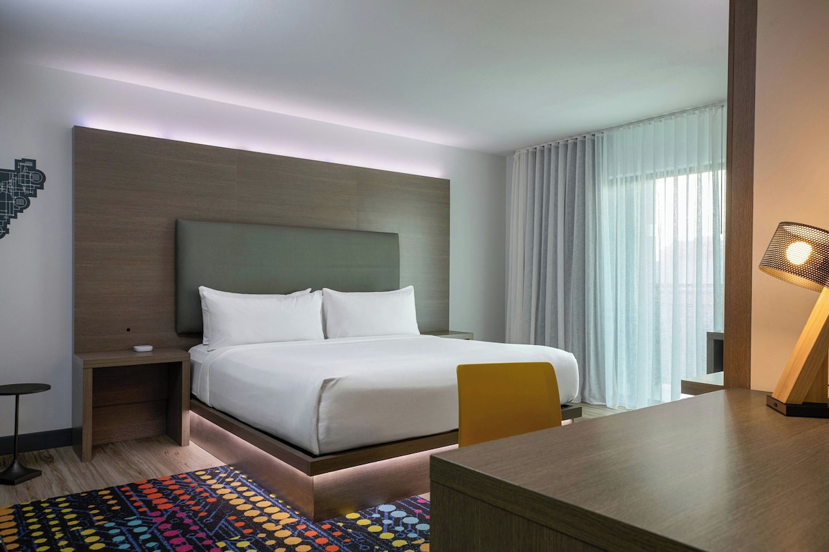 A modern hotel room with a large bed, a desk, and a chair.