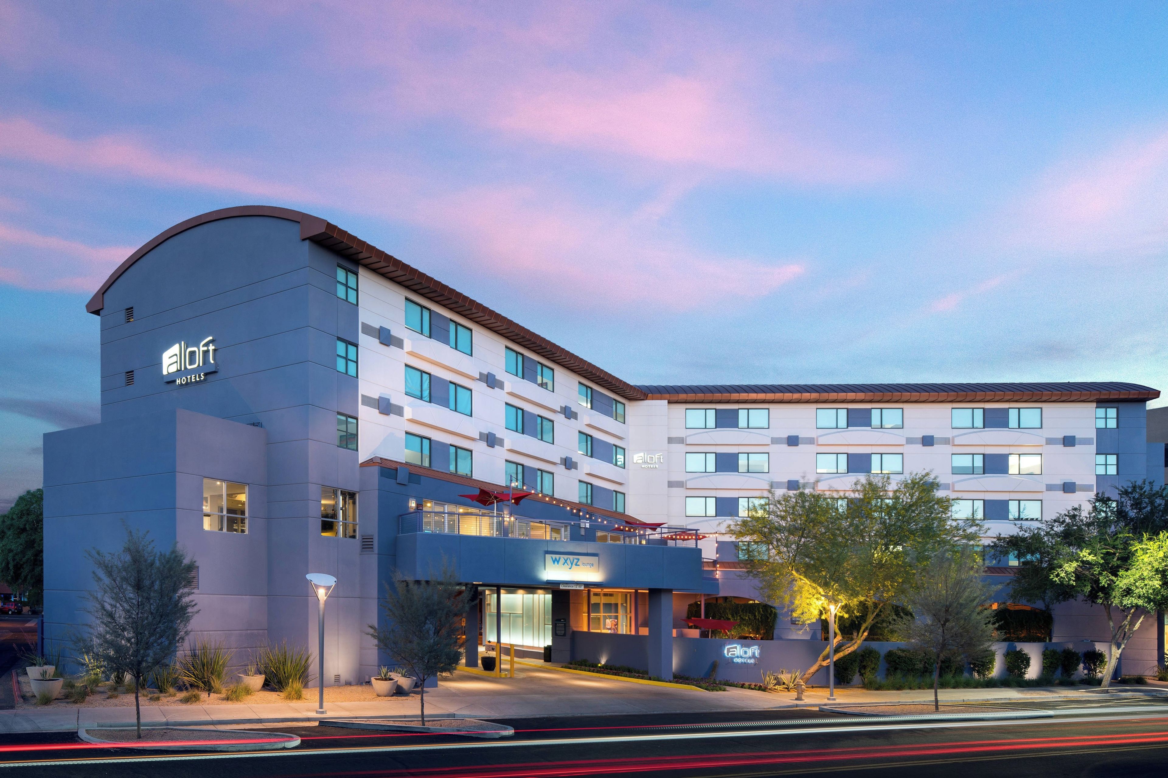 A modern hotel building with multiple floors, a curved entrance, and a clear sky.