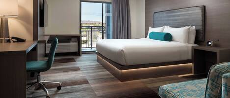A hotel room with a bed, a desk, a chair, a TV, and a view of the outdoors.