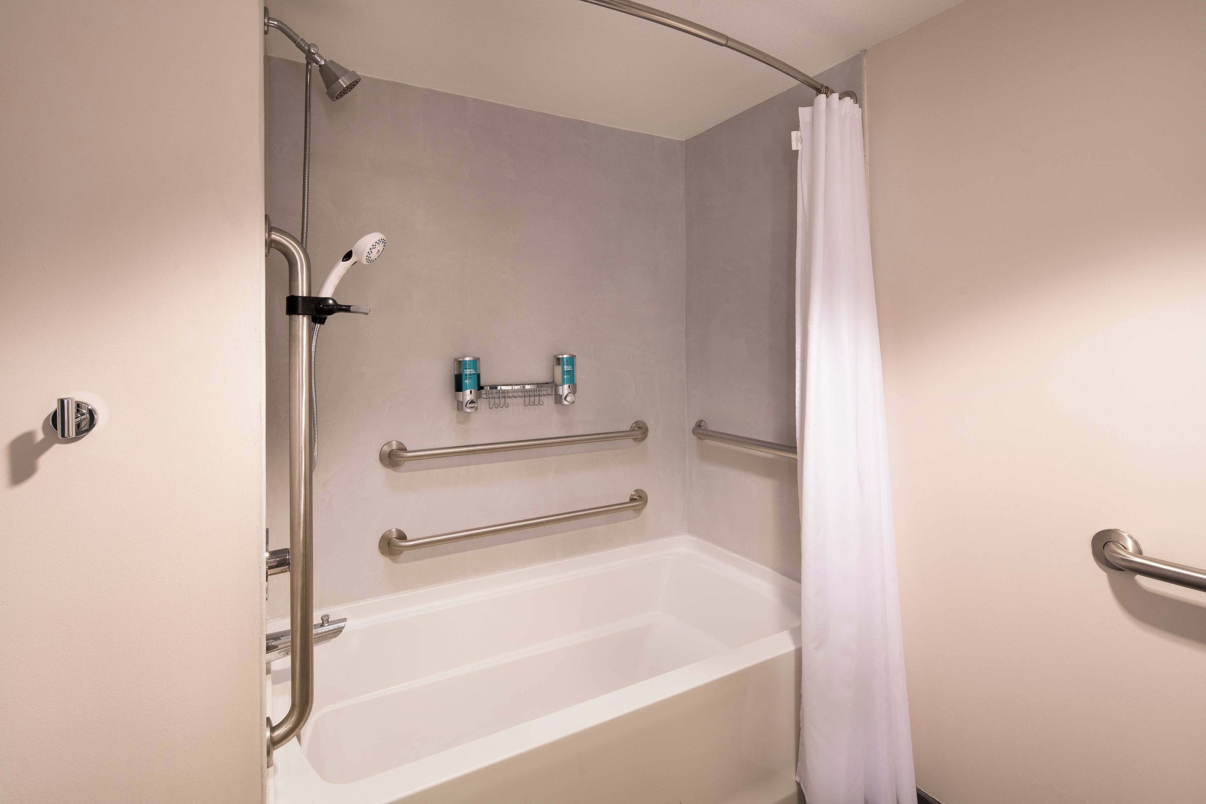 A standard hotel bathroom with a bathtub, shower, and handrails.