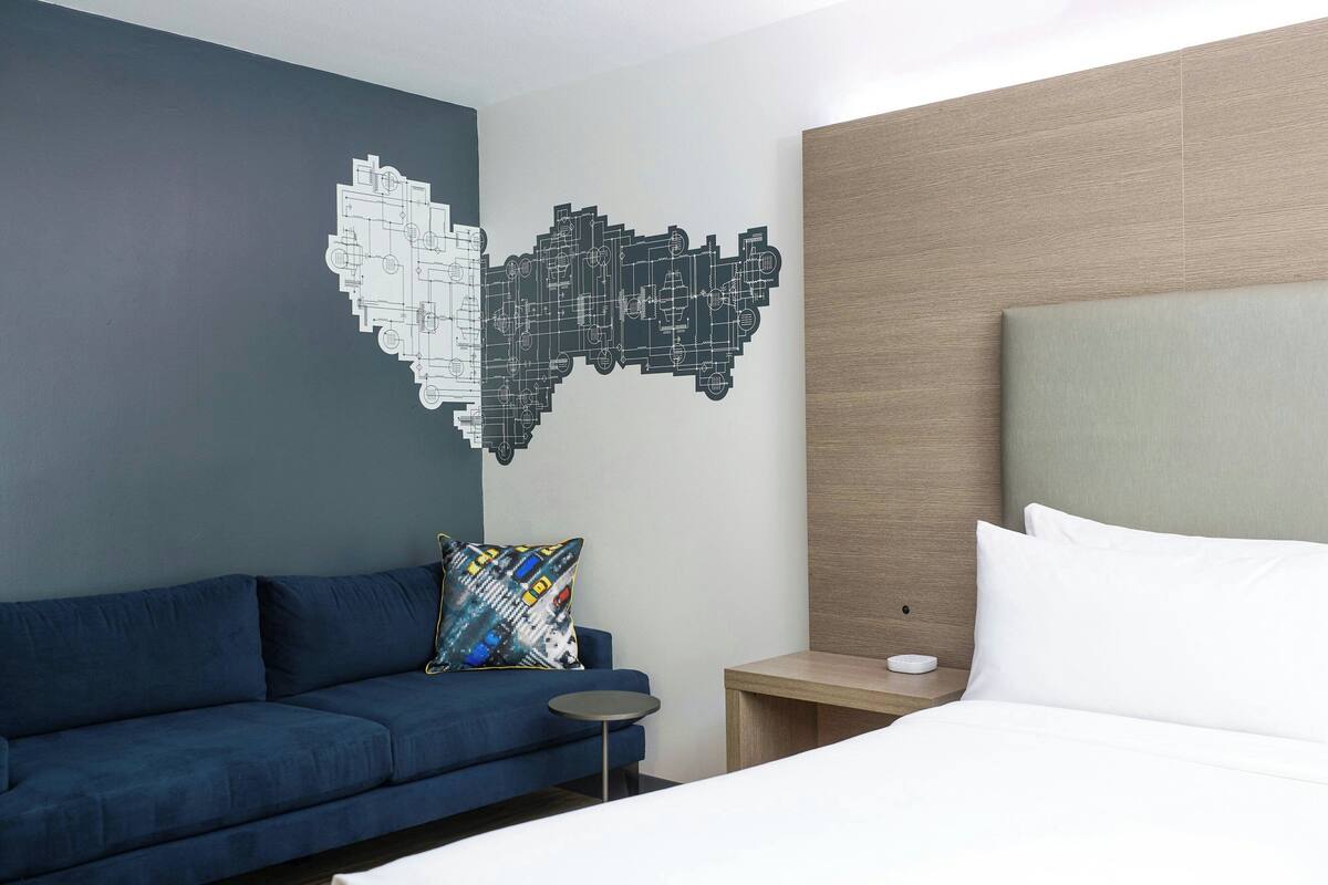 A hotel room with a blue sofa, a bed with white bedding, and a wall art piece.