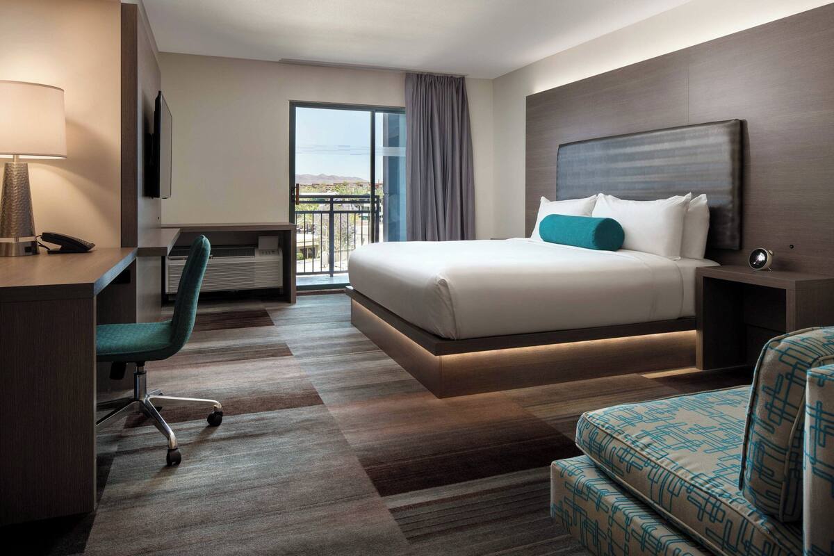 A hotel room with a bed, a desk, a chair, a TV, and a balcony with a view.