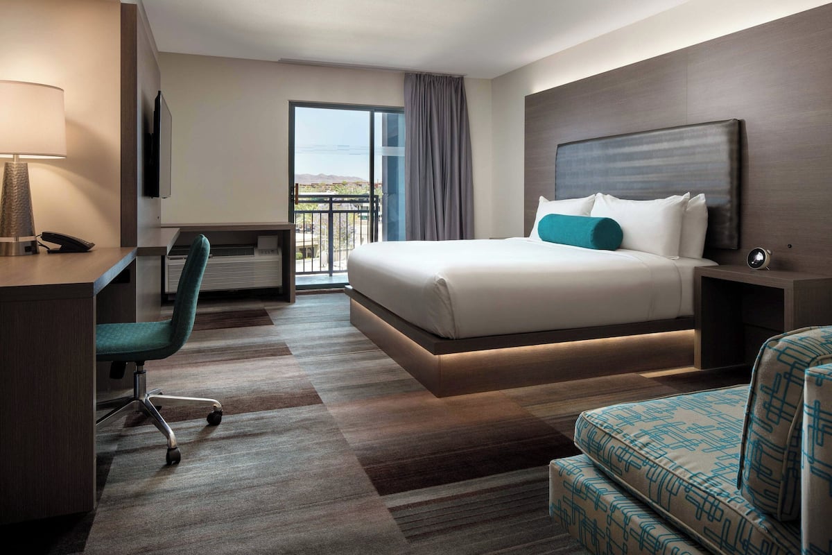 A hotel room with a bed, a desk, a chair, a TV, and a balcony with a view.