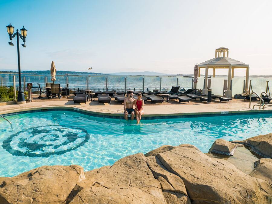 A pool area with lounge chairs, a gazebo, and a view of the sea.