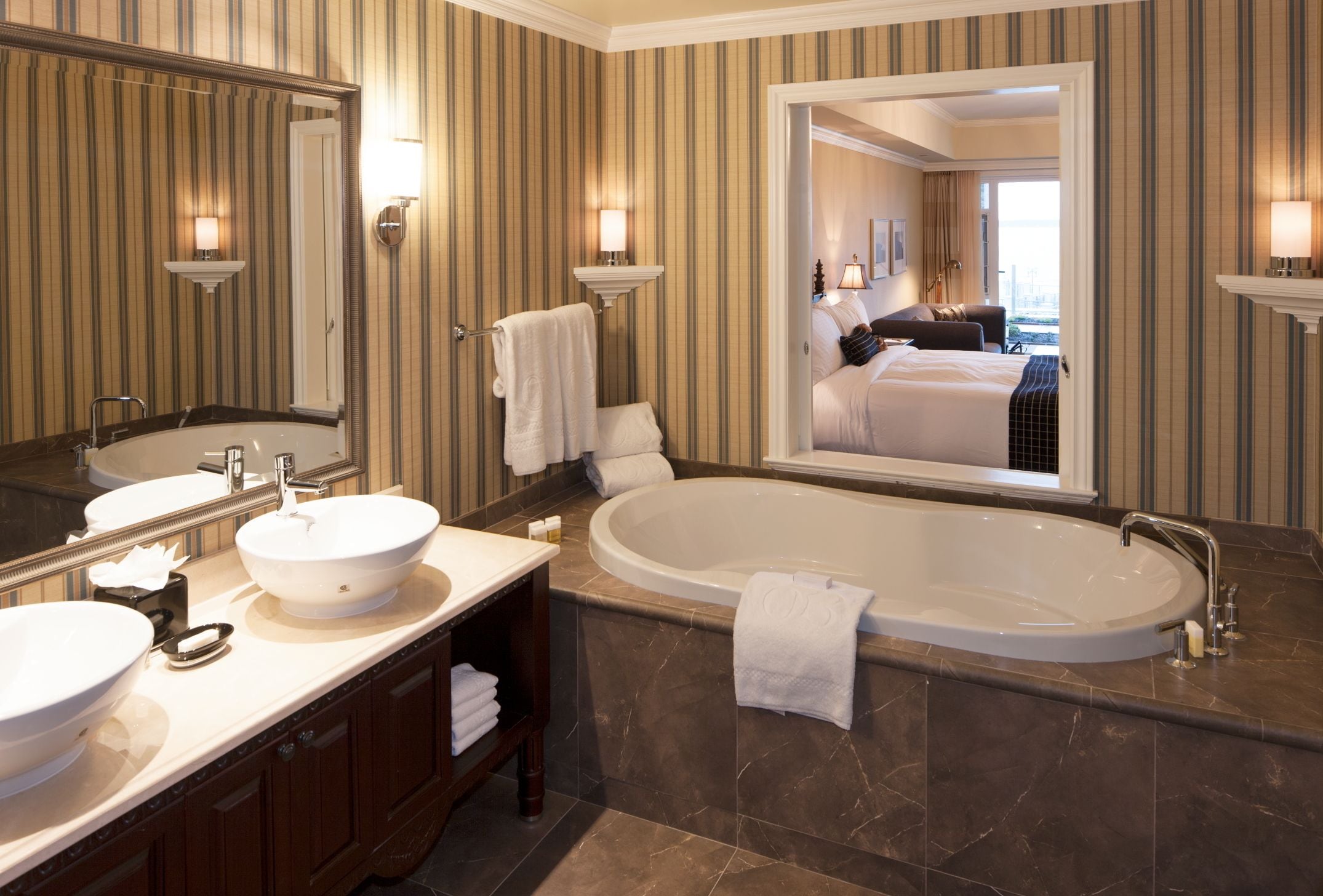 A hotel bathroom with two sinks, a large bathtub, and a mirror reflecting the room.