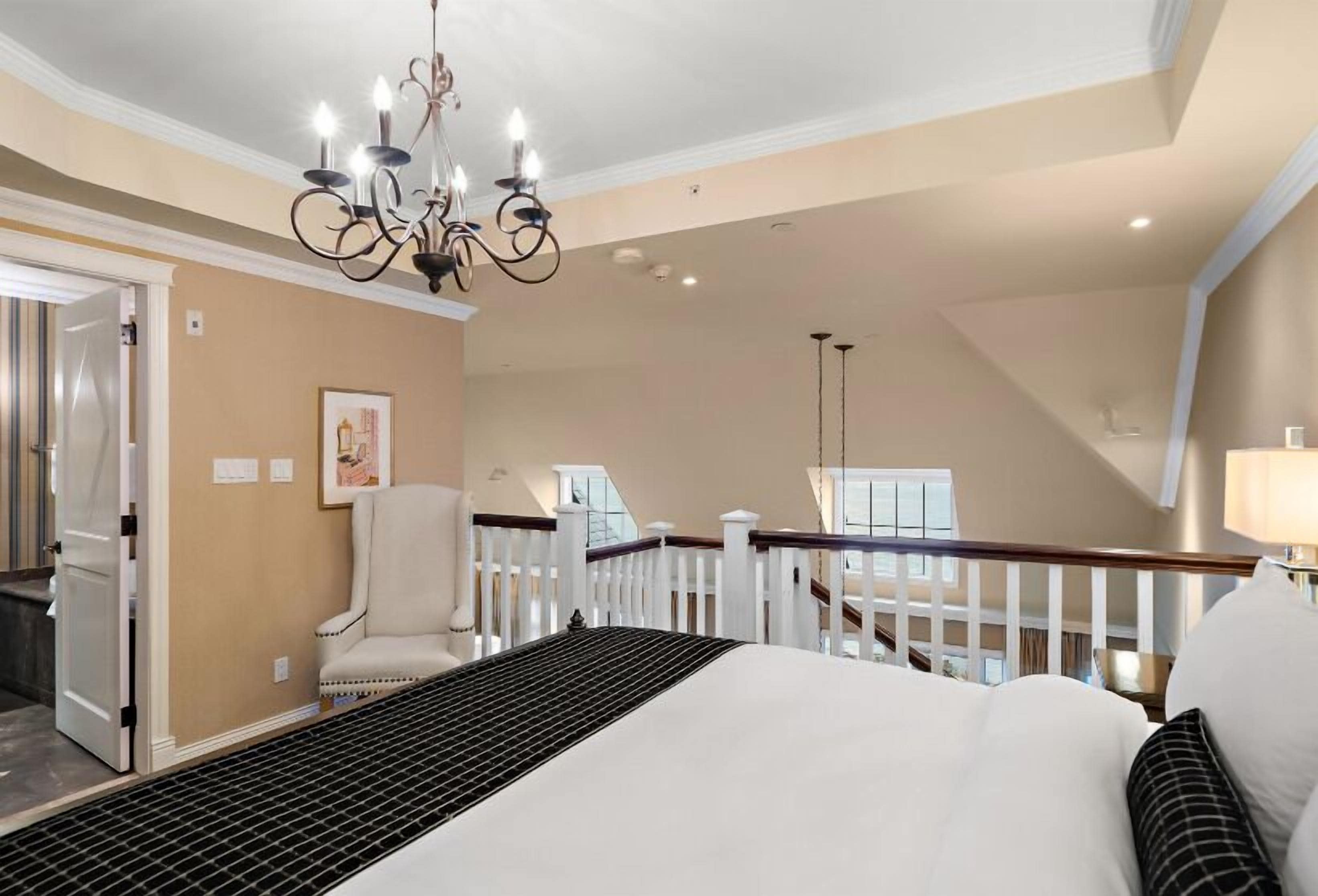 Un dormitorio espacioso con una cama grande, una araña de cristal, una barandilla blanca y vistas al balcón.