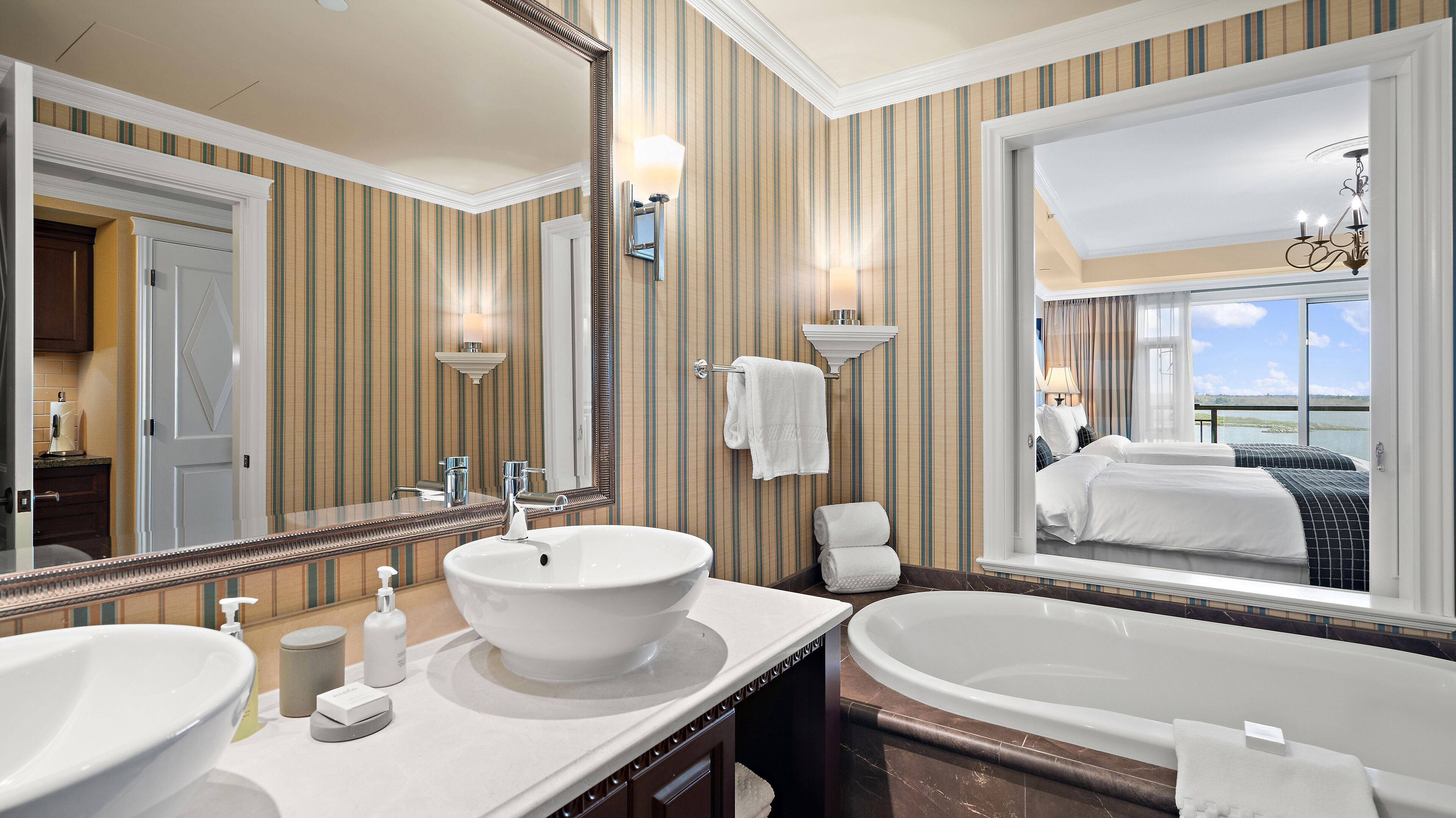 A hotel bathroom with two sinks, a large mirror, and a view of the room.