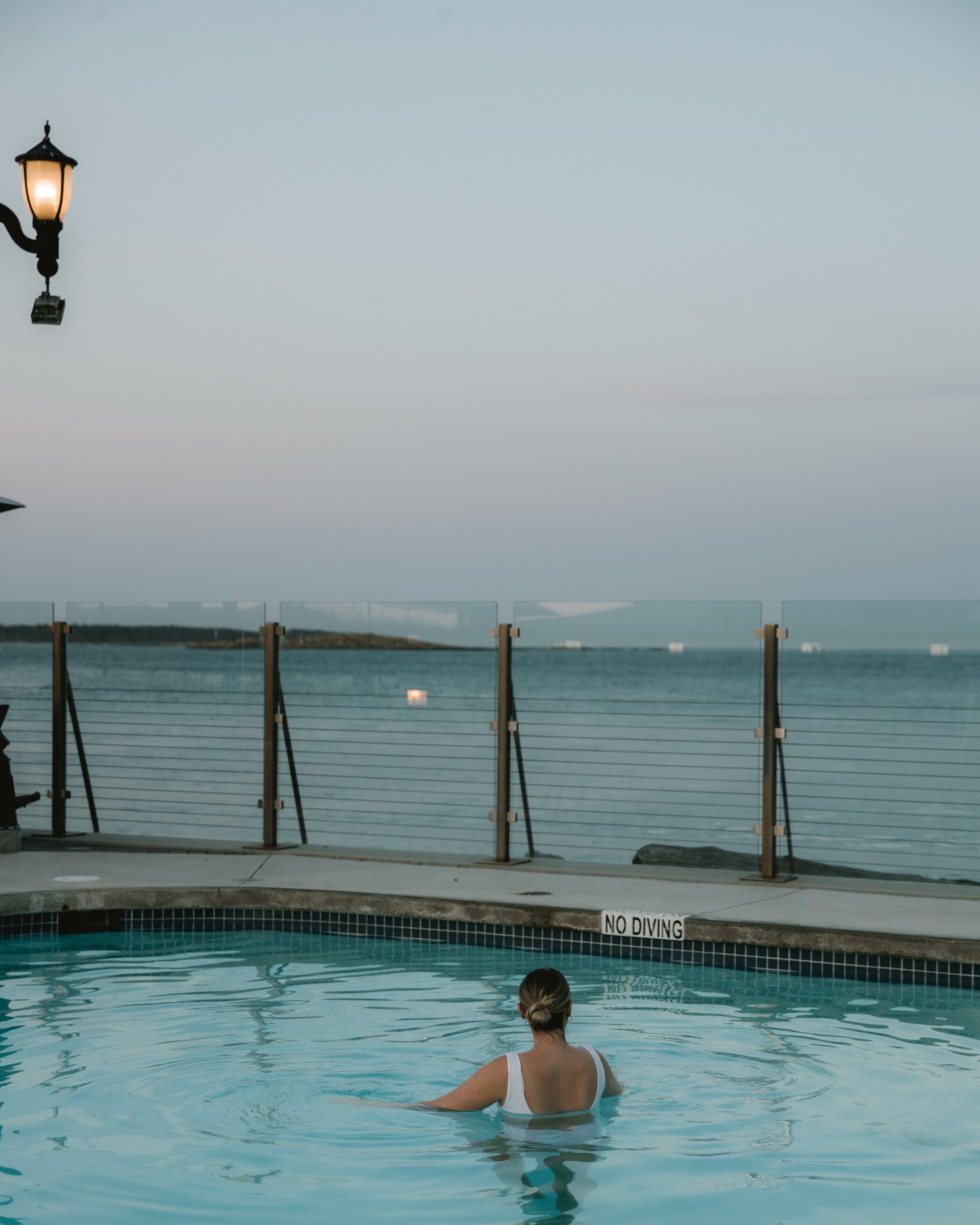 Une piscine avec un panneau indiquant « Il est interdit de plonger », un lampadaire et une vue sur la mer.