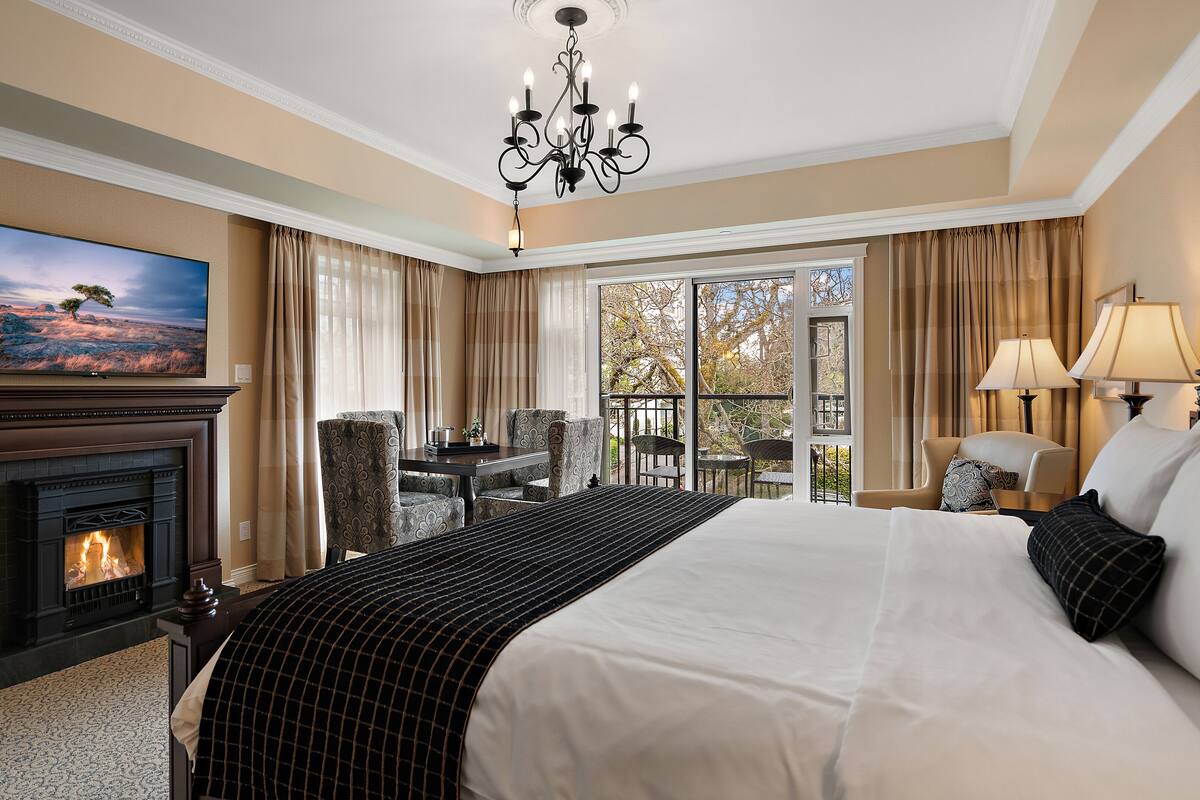 Ein Hotelzimmer mit Kamin, einem großen Bett, einem Fernseher, einem Balkon mit Sitzgelegenheiten und einer Kristallleuchtre.