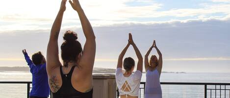 Un grupo de personas practicando yoga en un balcón con vista al mar.