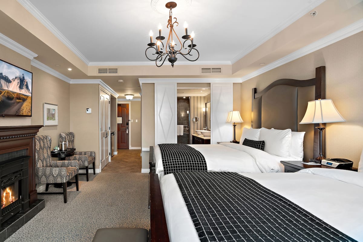 Ein Hotelzimmer mit Kamin, einem großen Bett, einem Schreibtisch mit Lampe und einem durchgehenden Türbogen einsehbaren Badezimmer.