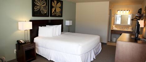 Une chambre d’hôtel avec un grand lit, des tables de chevet, un bureau et une salle de bain équipée d’un lavabo et d’un miroir.