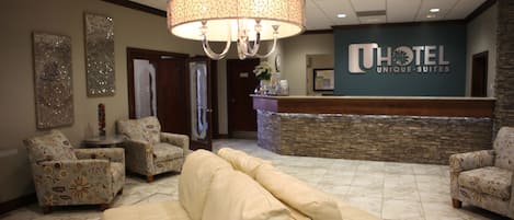 A hotel lobby with a reception desk, patterned armchairs, a beige sofa, and a chandelier.