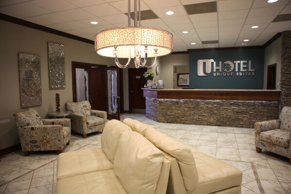 A hotel lobby with a reception desk, patterned armchairs, a beige sofa, and a chandelier.