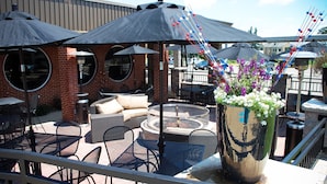 An outdoor patio with round tables and chairs, a fire pit, and umbrellas providing shade. - Unique Suites Hotel (Charleston)