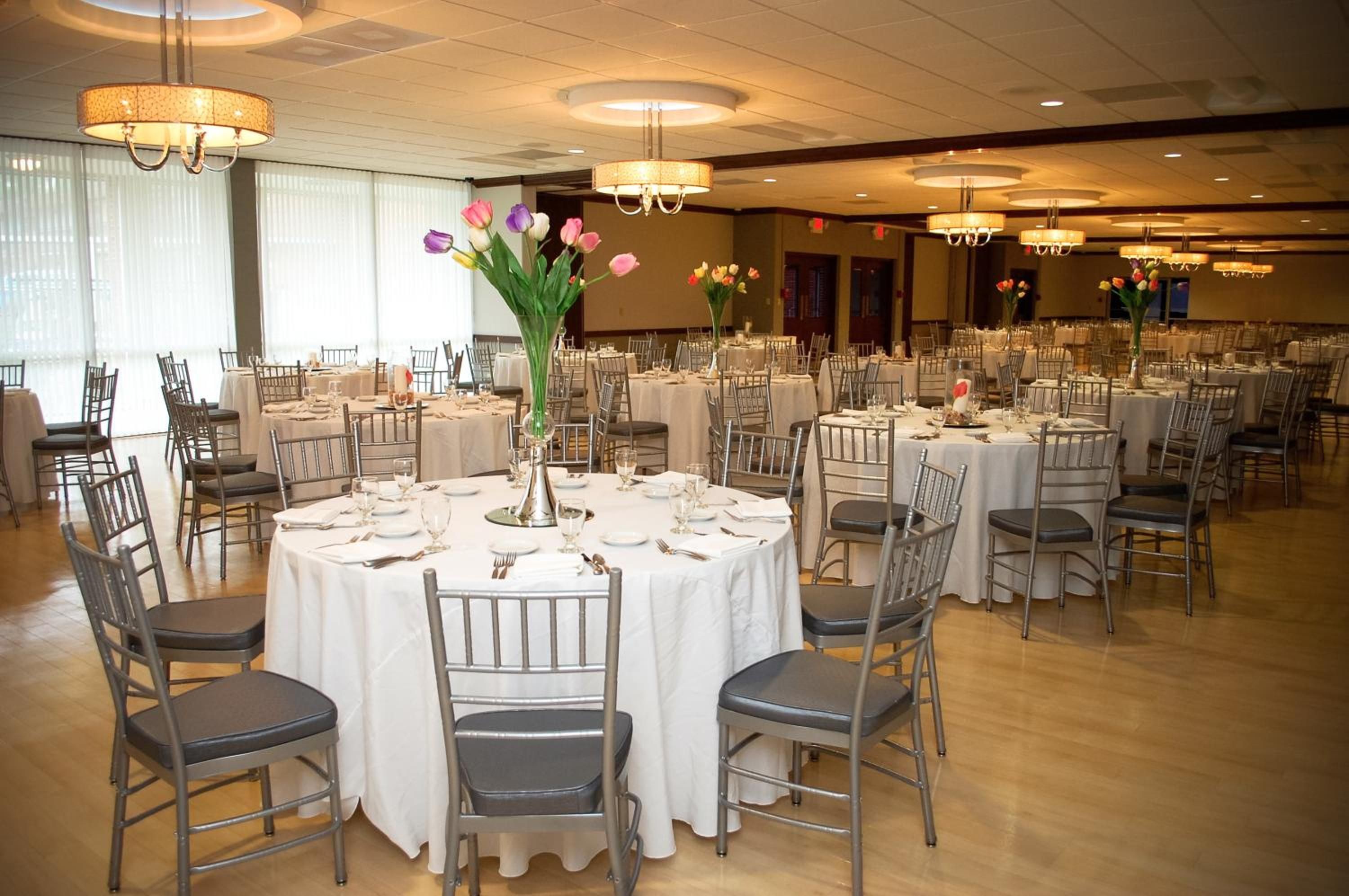 A banquet hall with round tables, chairs, and chandeliers.