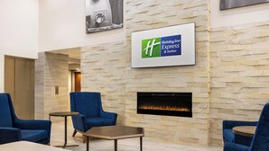 Vestíbulo de Holiday Inn Express & Suites con paredes de piedra, chimenea y asientos azules.