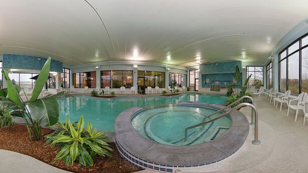 Una piscina interior con un jacuzzi, rodeada de sillas de descanso y plantas en macetas.