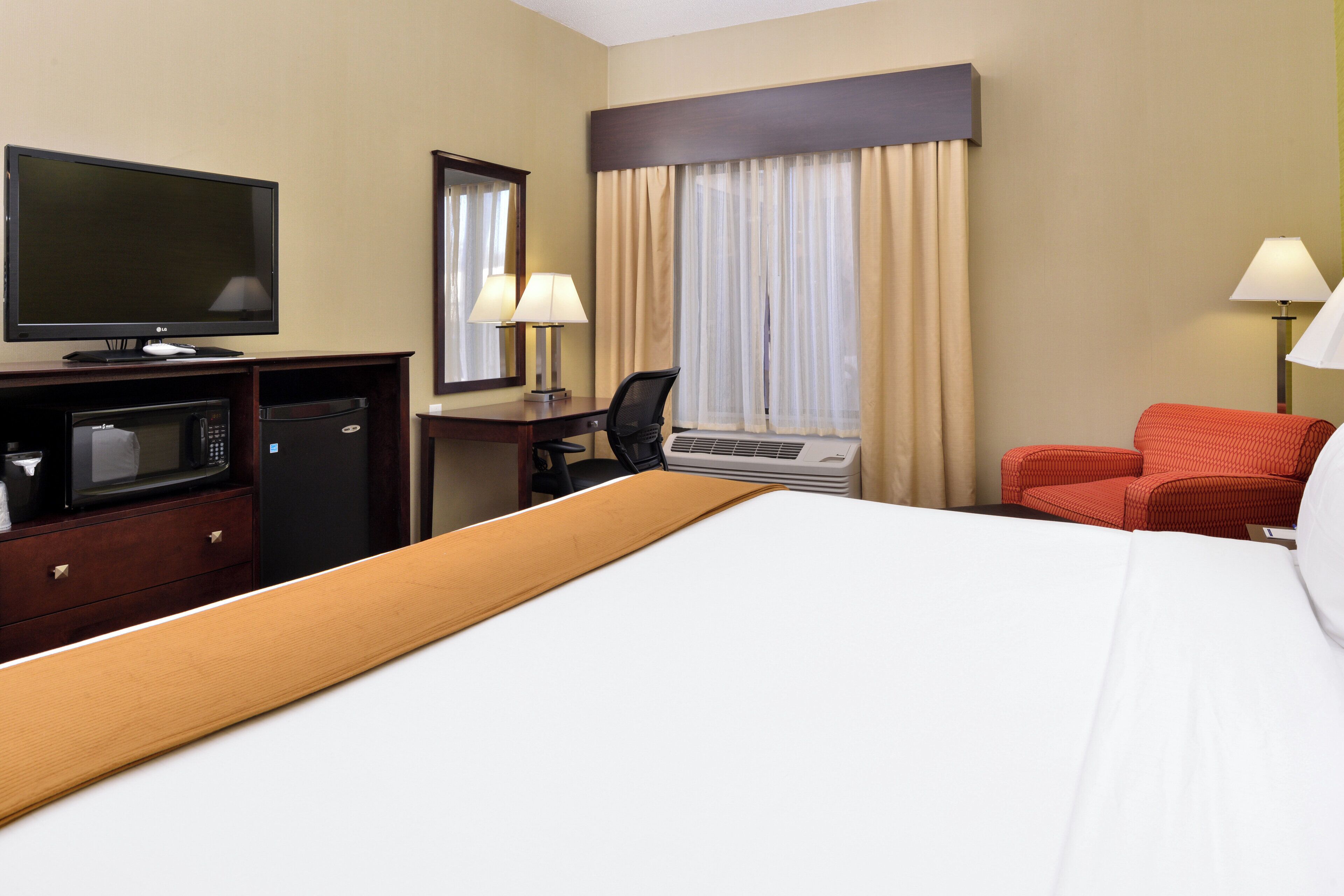 A hotel room with a bed, a desk with a computer, a television, a microwave, and a red sofa.