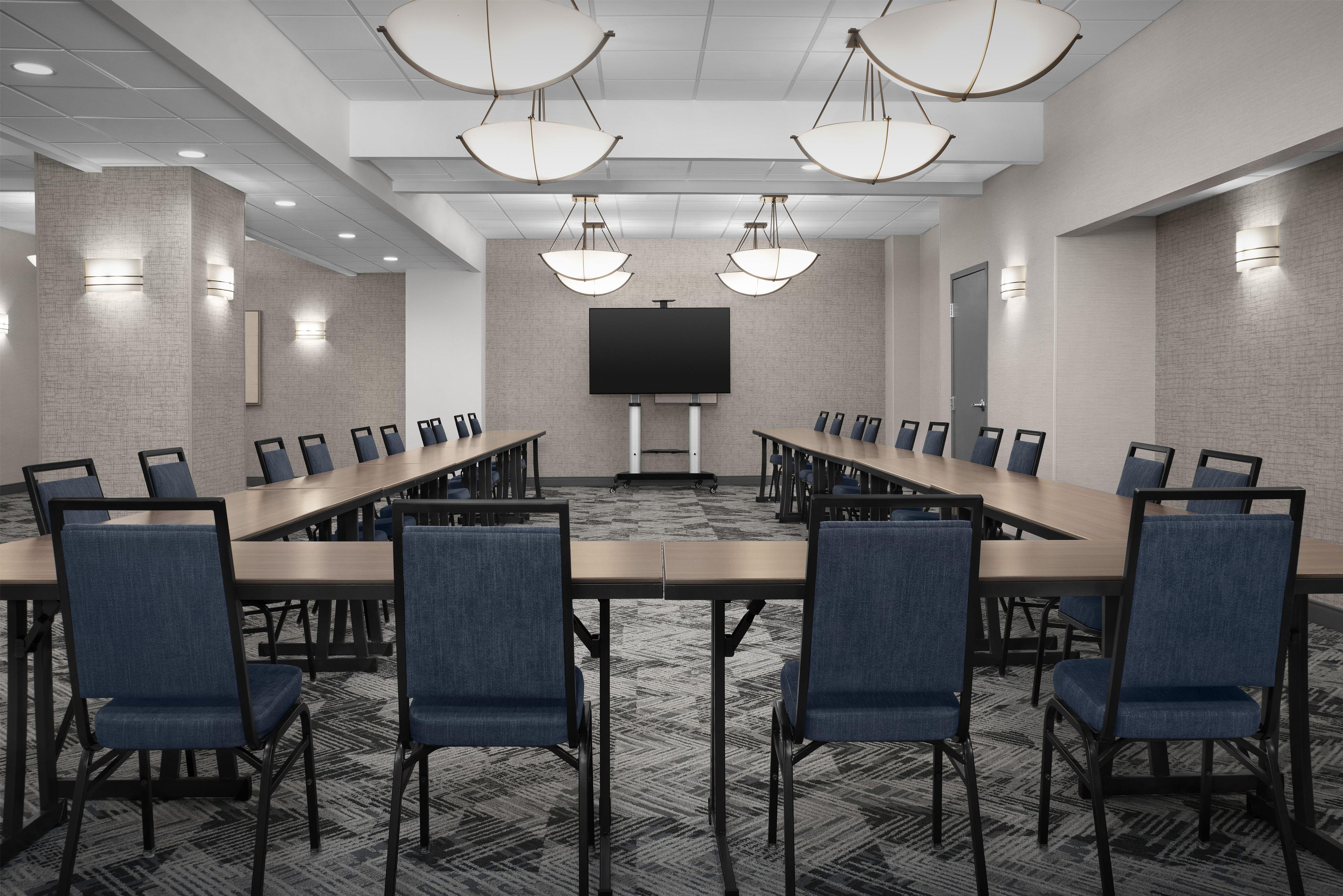 A conference room with a long table, chairs, a large screen, and pendant lighting.