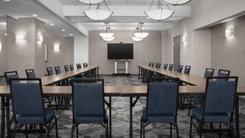 A conference room with a long table, chairs, a large screen, and pendant lighting.