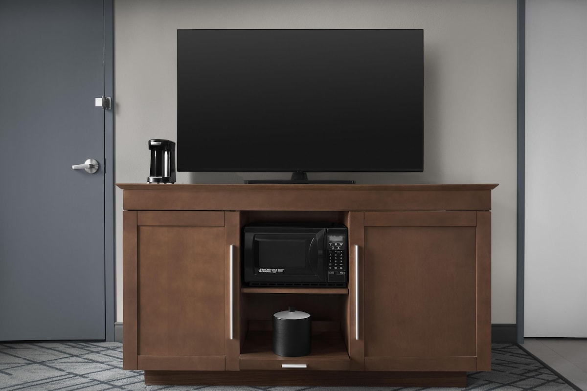 A modern kitchen with a built-in microwave, a coffee maker, and a flat-screen TV on a wooden cabinet.