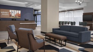 A modern hotel lobby with a reception desk, seating area, and a large TV screen.