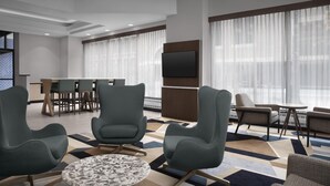 A modern hotel lobby with a dining area, comfortable seating, and a large TV screen.