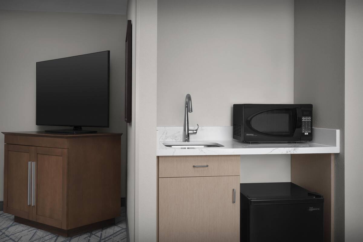 Eine kompakte Küchenzeile mit Flachbildfernseher, Mikrowelle, Spüle und kleinem Kühlschrank.
