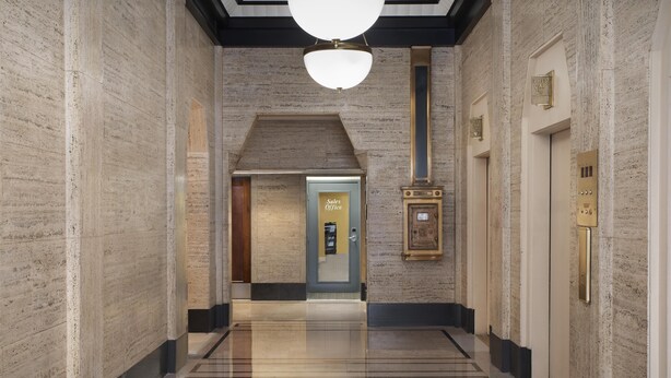 A polished hallway with marble walls, a modern light fixture, and an elevator with a brass plate.