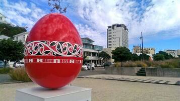 A large red egg sculpture with intricate white patterns on a white pedestal, set against a backdrop of buildings and a clear sky.